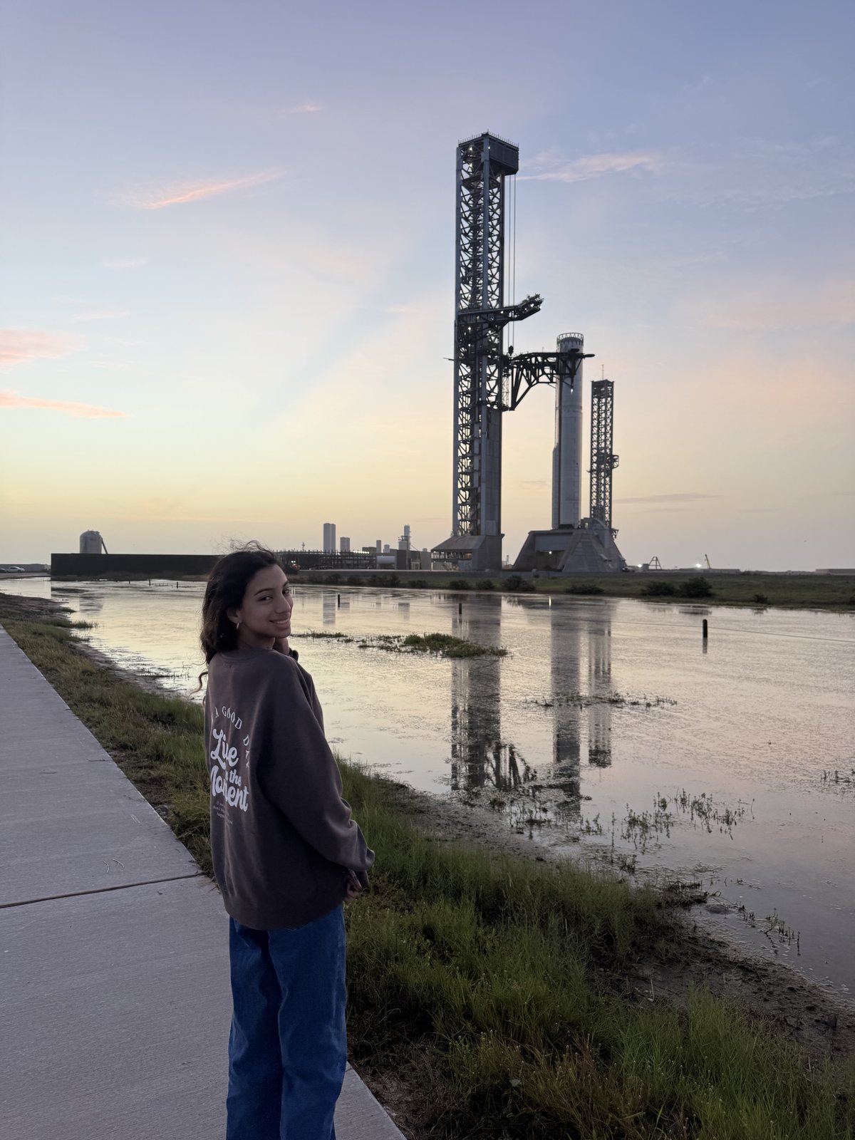 Saanvi Phaneendra at sunrise in front of the Starship launch tower and Super Heavy Booster 20, reflected in the water at Starbase, Texas