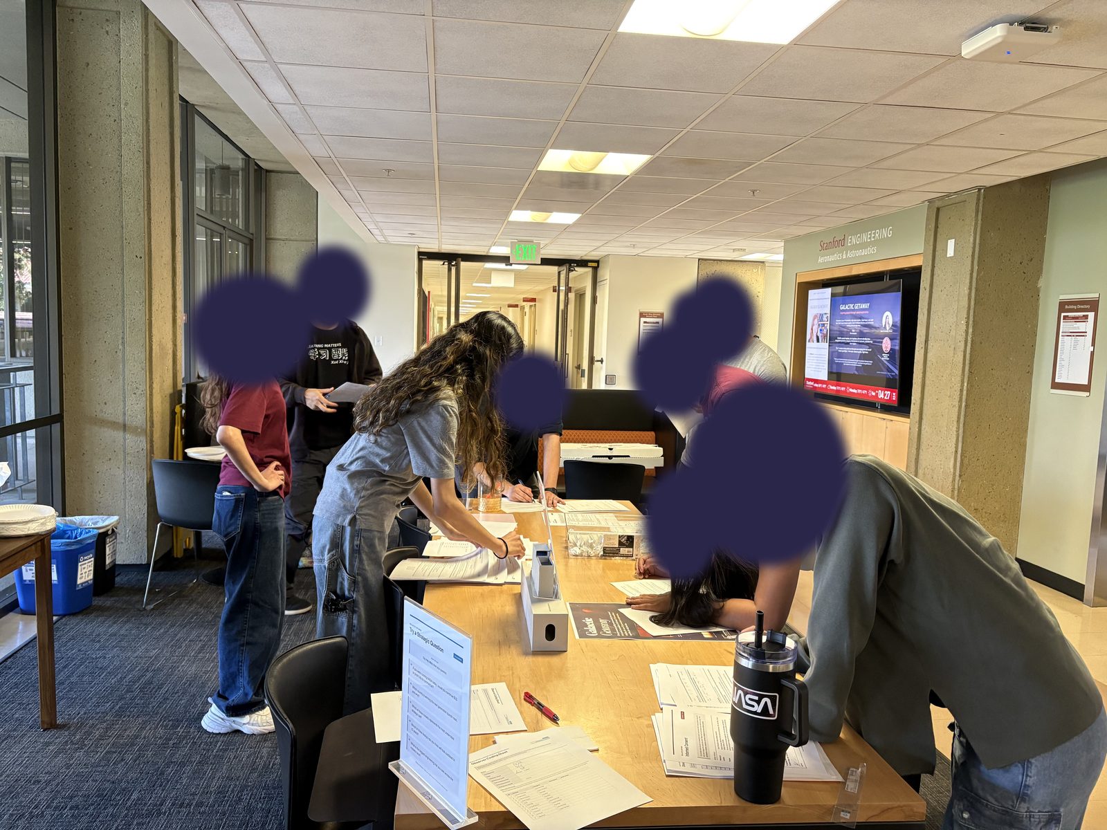 A group of participants leaning over a long table, filling out survey forms. Faces are covered.